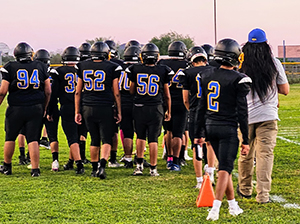 Football team raising their helmets up as they stand together on a field